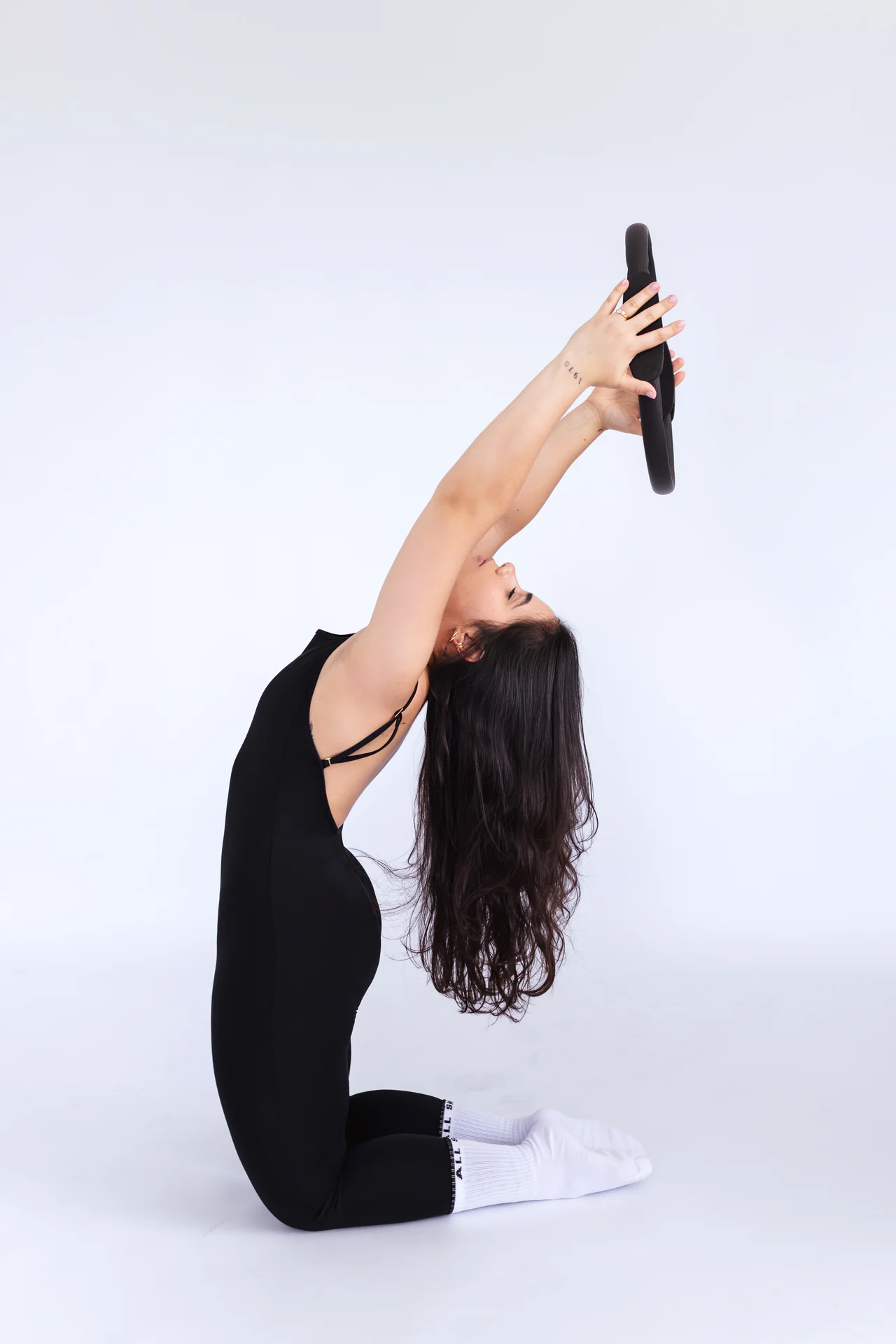Yndinajara ajoelhada, segurando um arco acima da cabeça em uma pose de exercício.